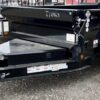 Black Iron Bull dump trailer with dual axles parked on gravel lot with other trailers visible in background.