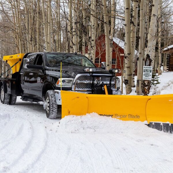 Black pickup truck equipped with a large yellow snow plow and a yellow salt spreader on the back, clearing snow on a snowy residential road