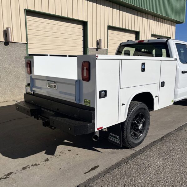 White pickup truck with black wheels and utility bed, parked outside a building with beige walls.