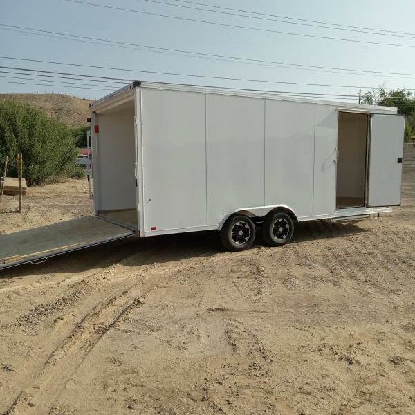 White enclosed cargo trailer with side door, rear ramp down, and dual axles on a dirt lot