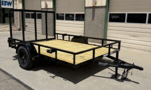 Utility trailer with a black frame and wood flooring sitting in the sun next to a closed multi-door garage at Pine Country.